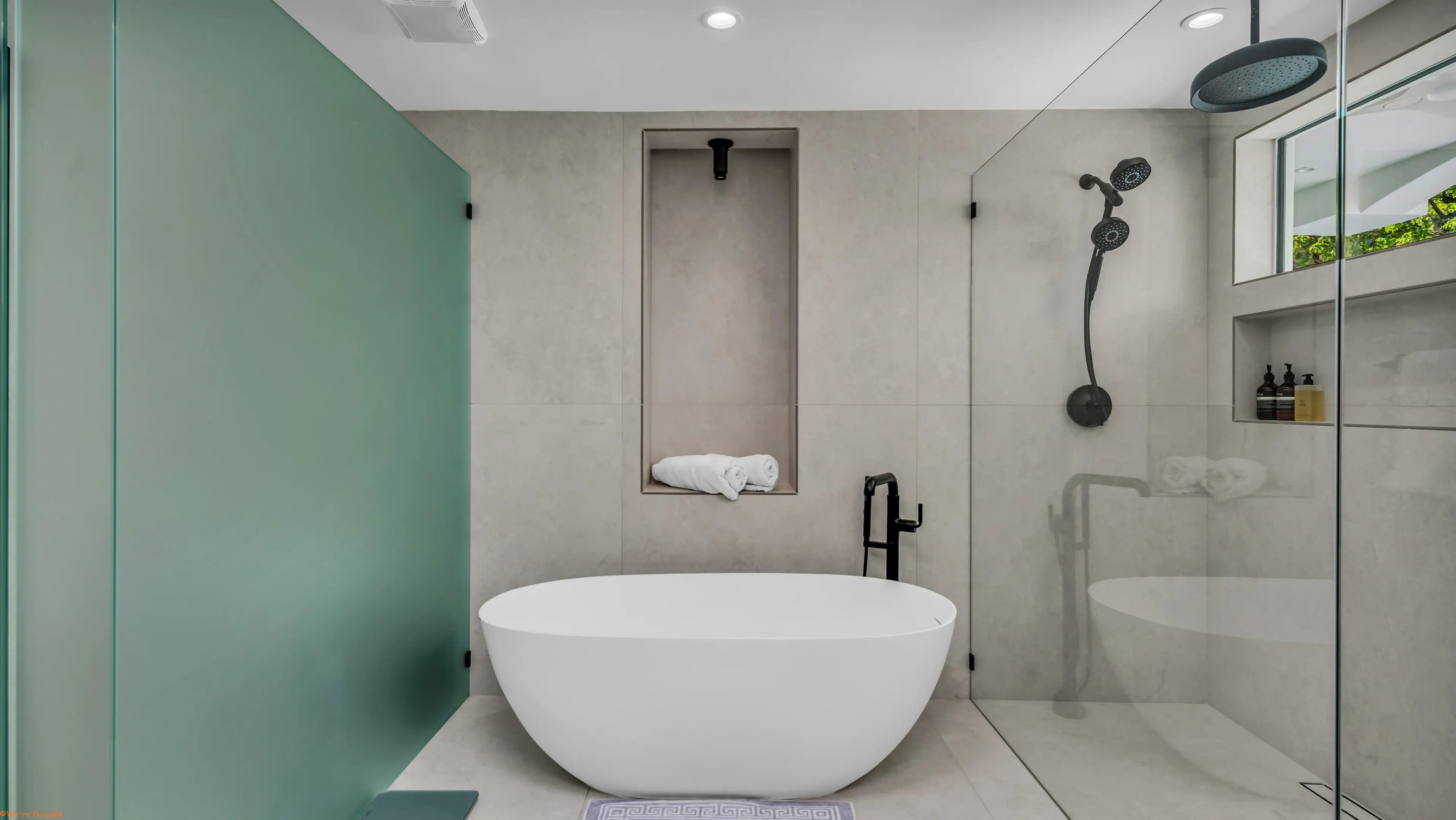 A freestanding tub against a sea green glass wall, with a walk in shower alongside.