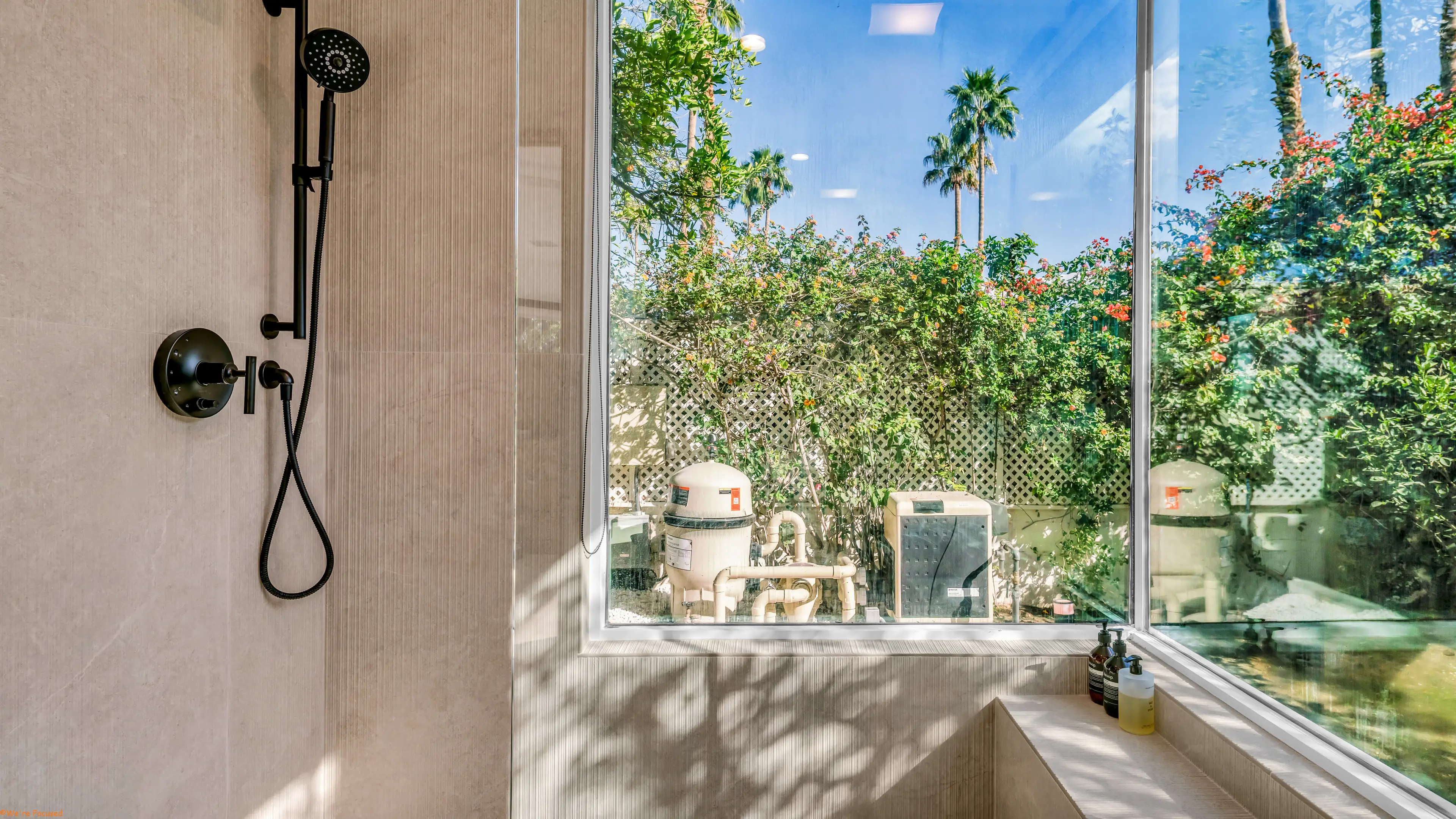 From inside the shower, a corner window filled with palms and greenery.