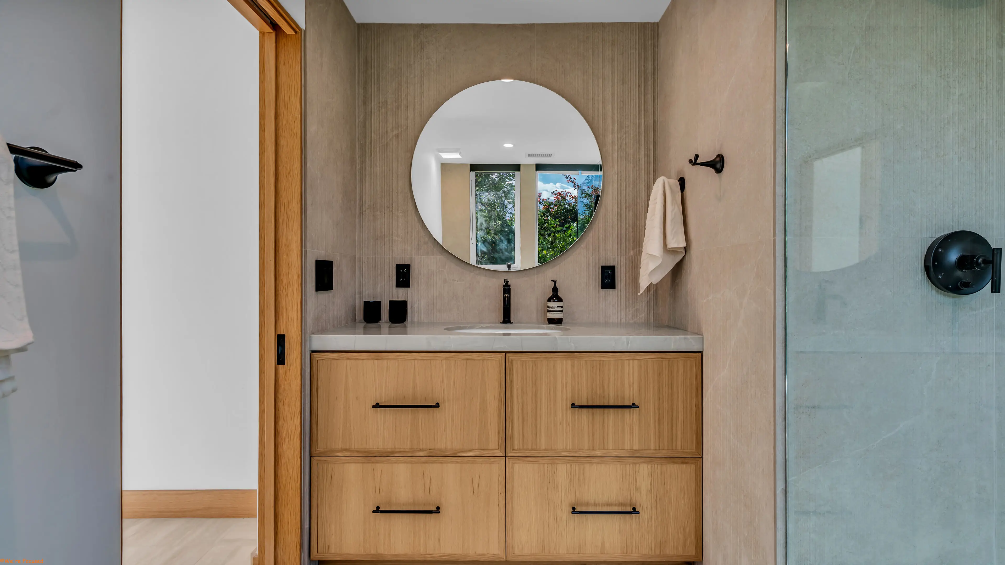 An oak vanity with a round mirror in a bathroom of pale plaster and stone.