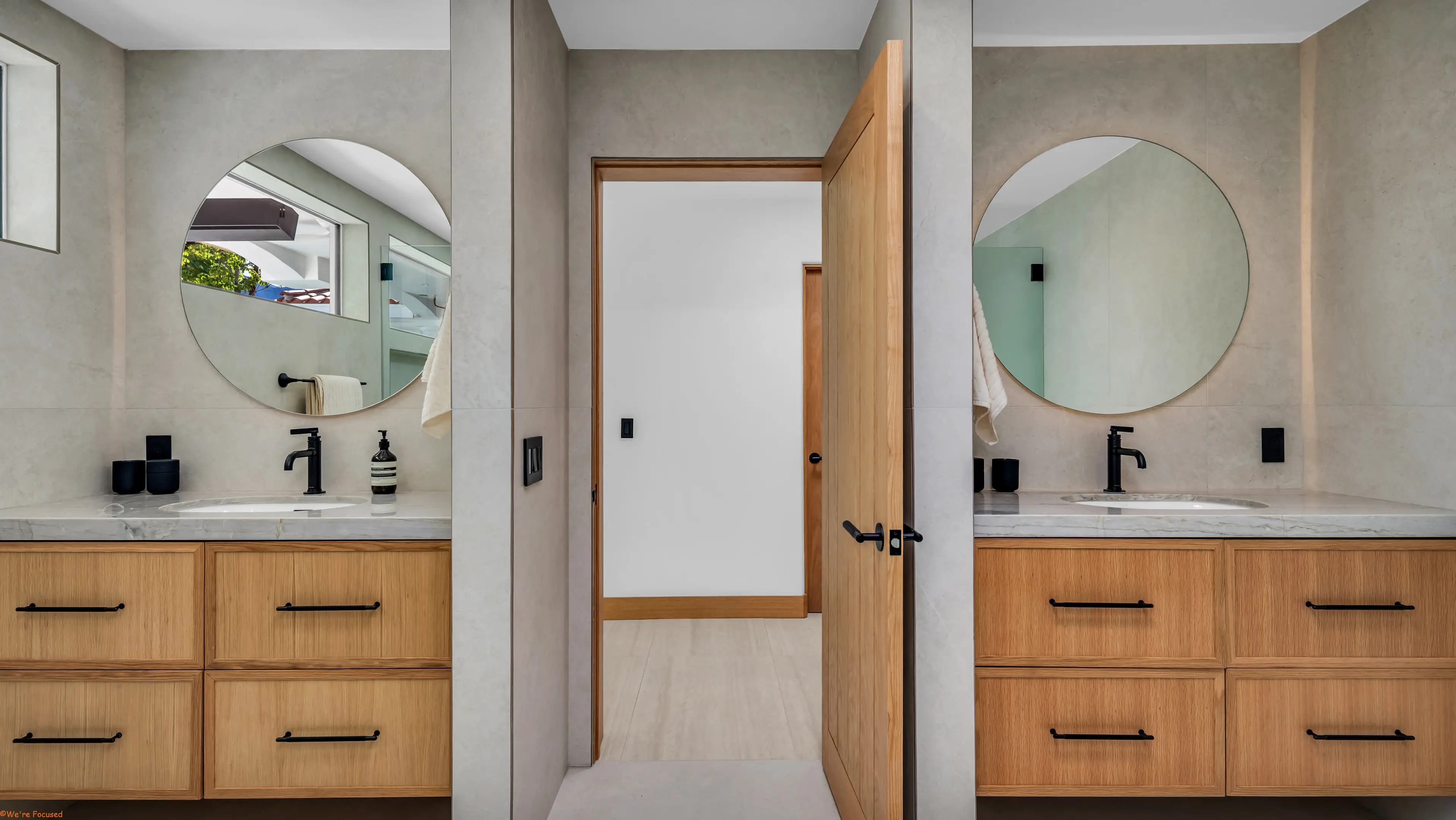Twin oak vanities with round mirrors either side of a doorway.