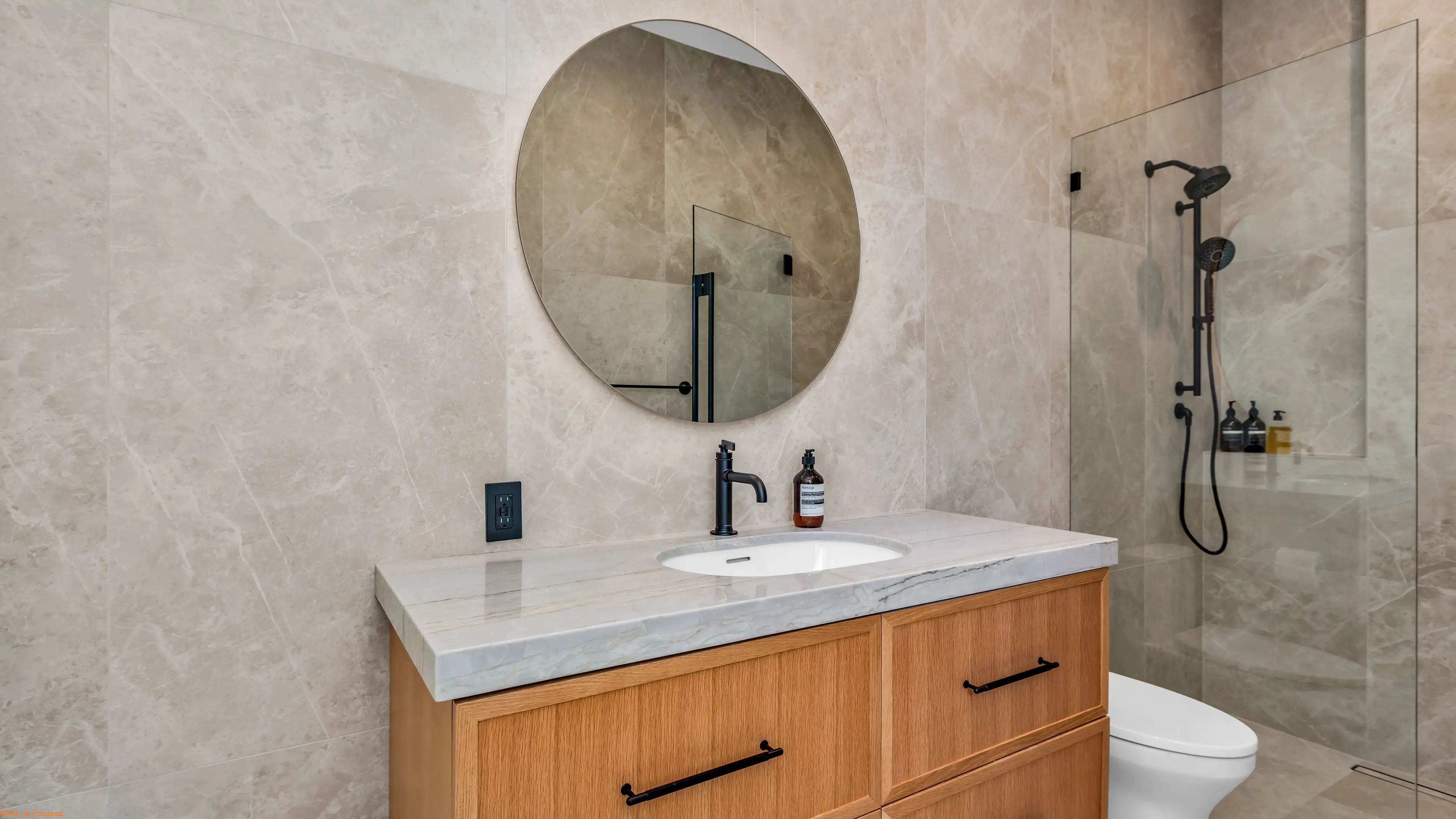 Vanity with a round mirror set against a full height stone wall, shower alongside.