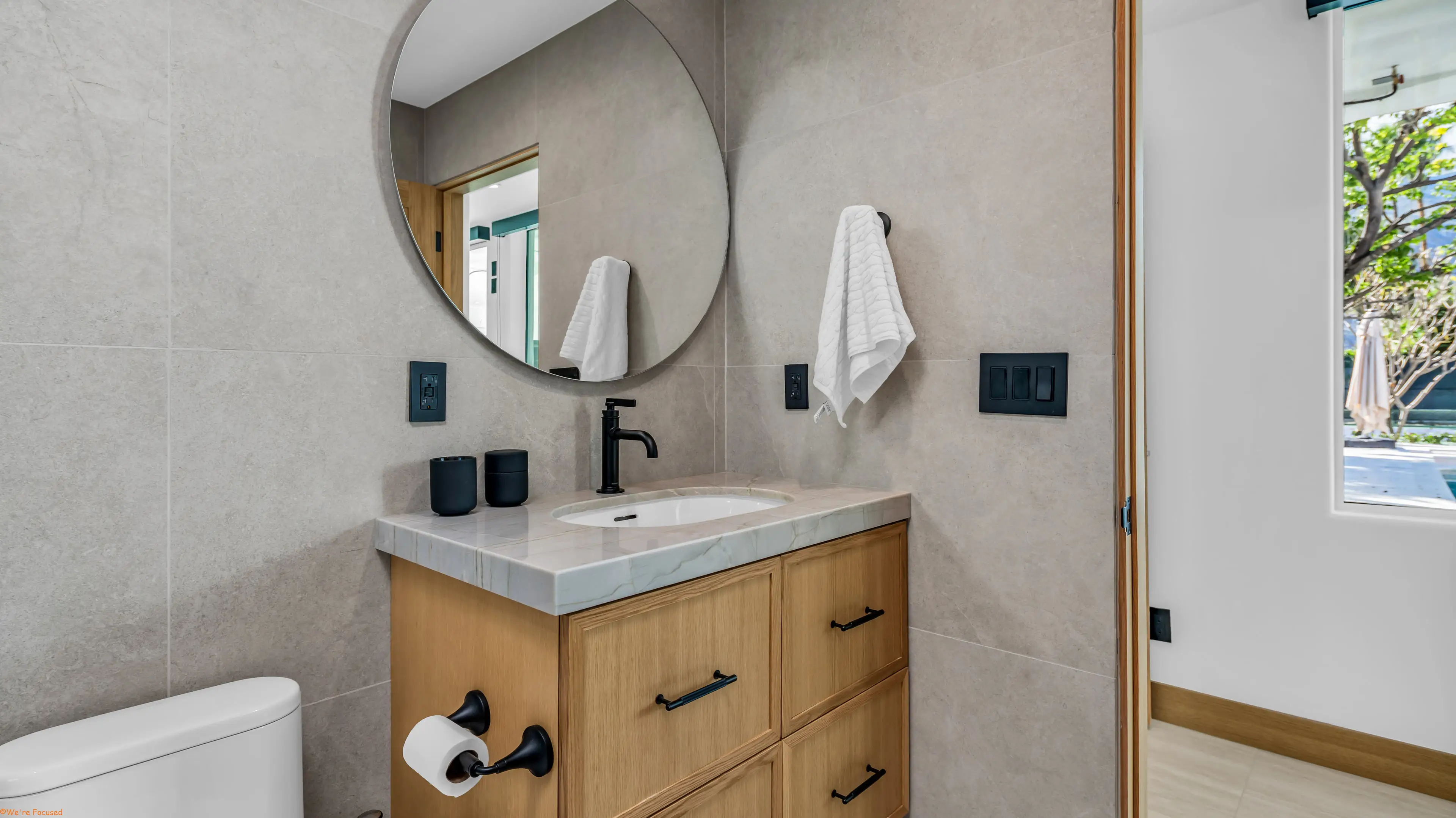 Vanity with a round mirror, black fittings and a folded towel on a ring.