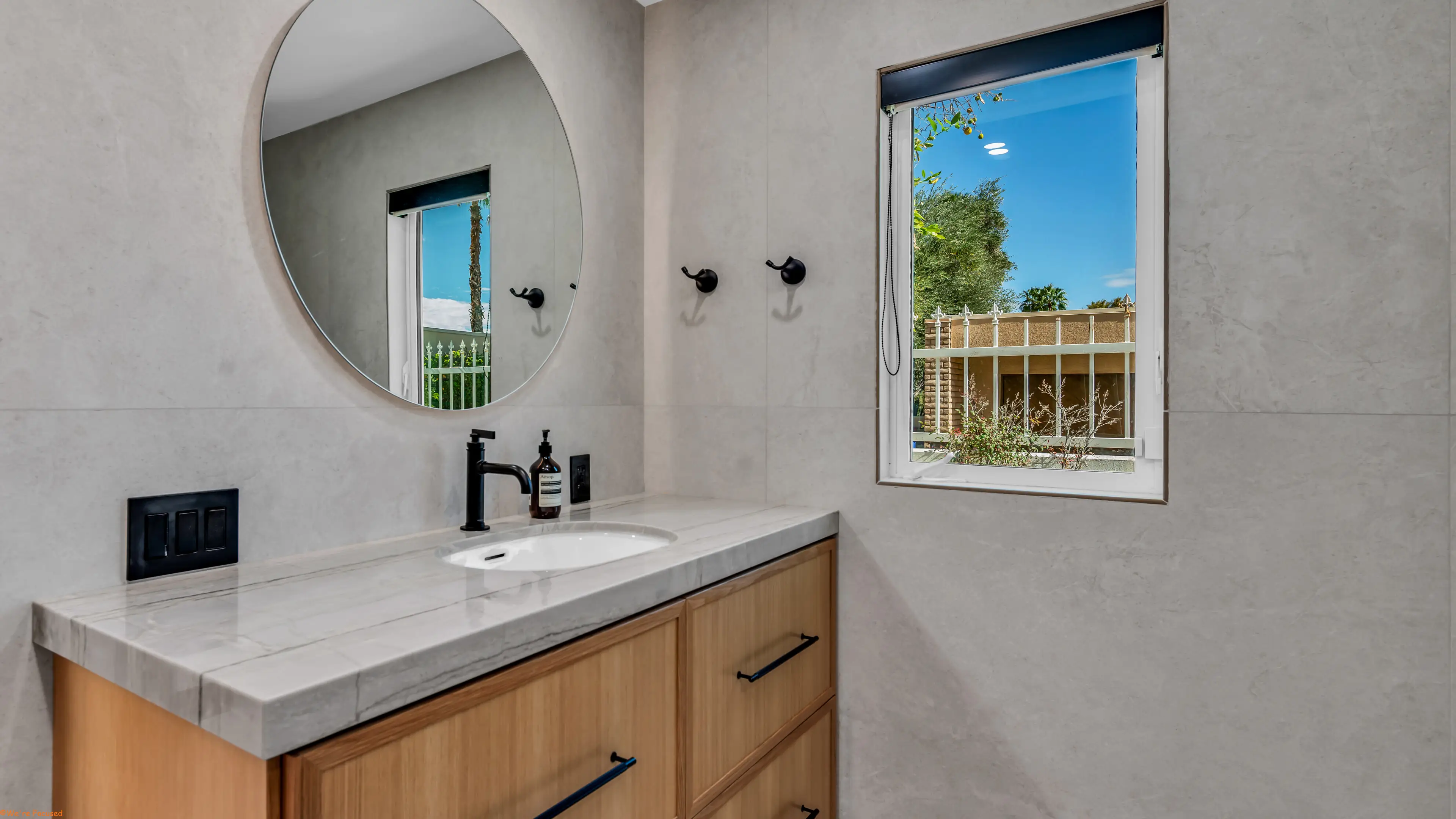 Vanity with a round mirror and a window looking onto the garden wall.