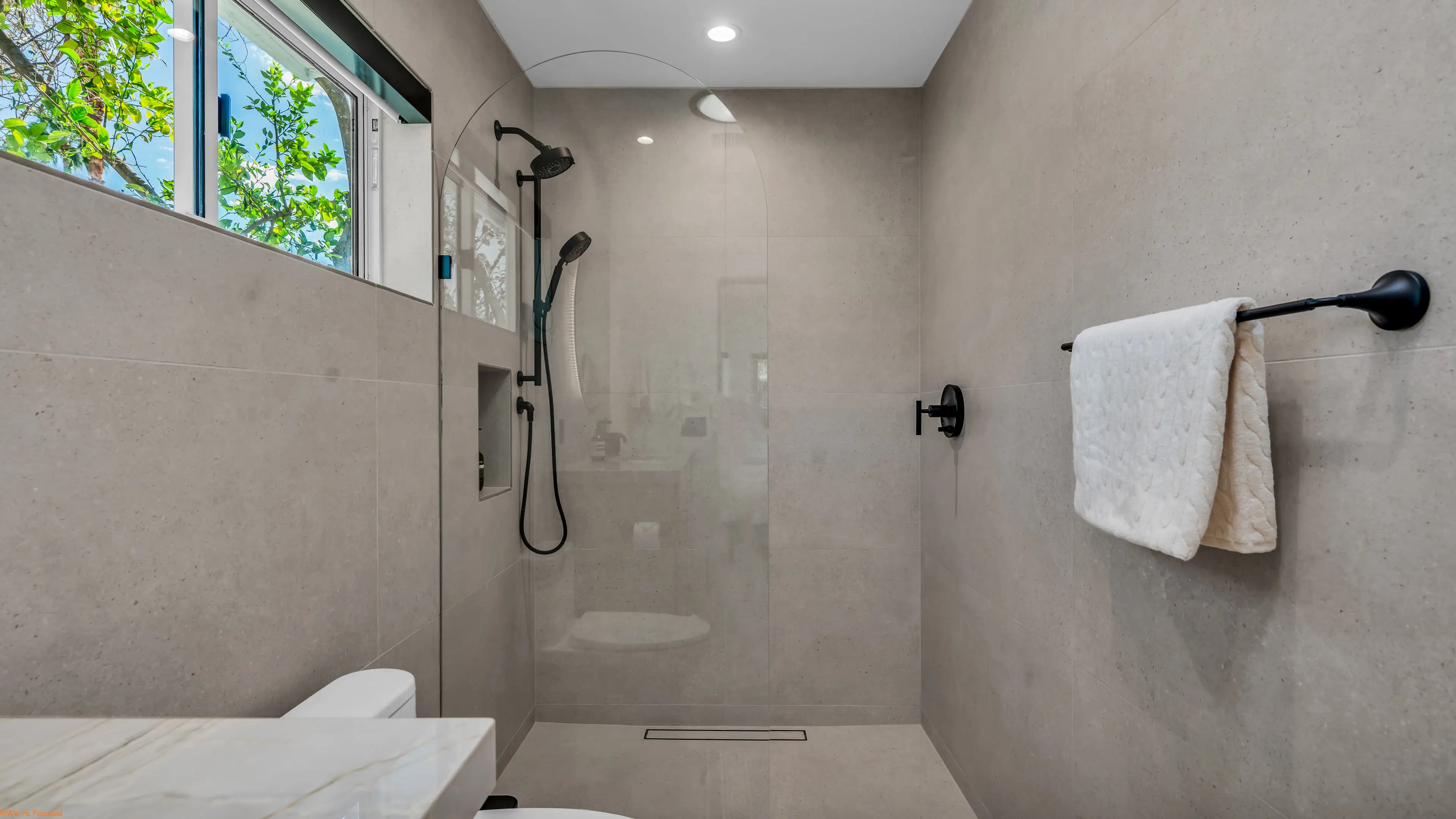 Walk in shower in pale stone tile with a window above.