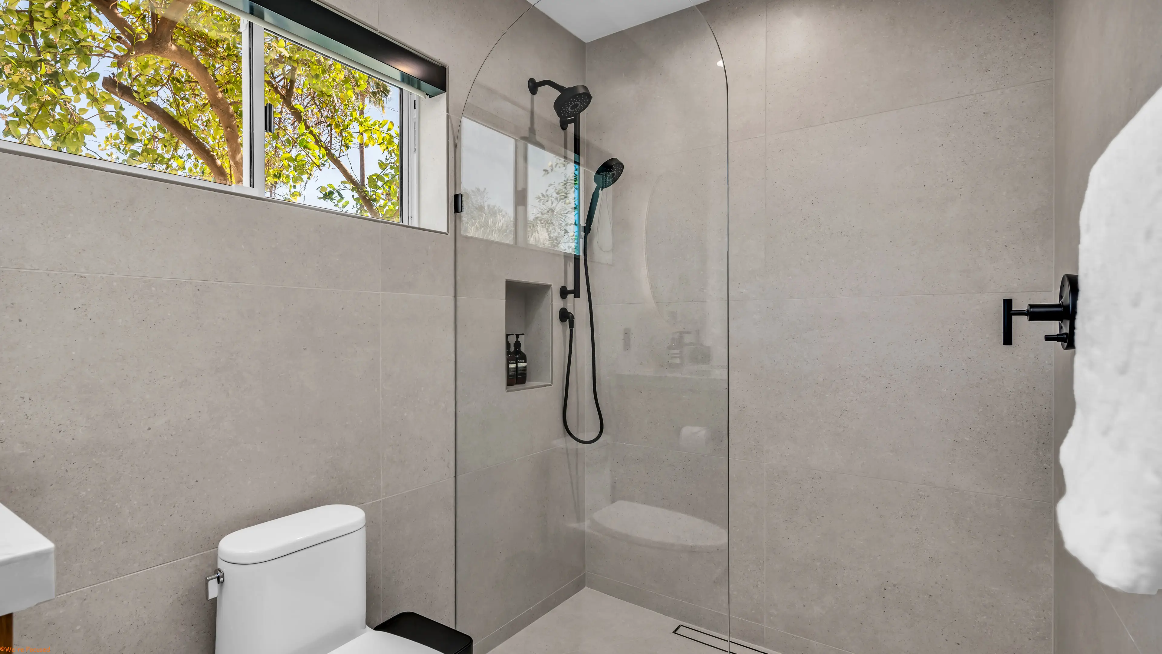 Walk in shower with a long window above and a garden view.