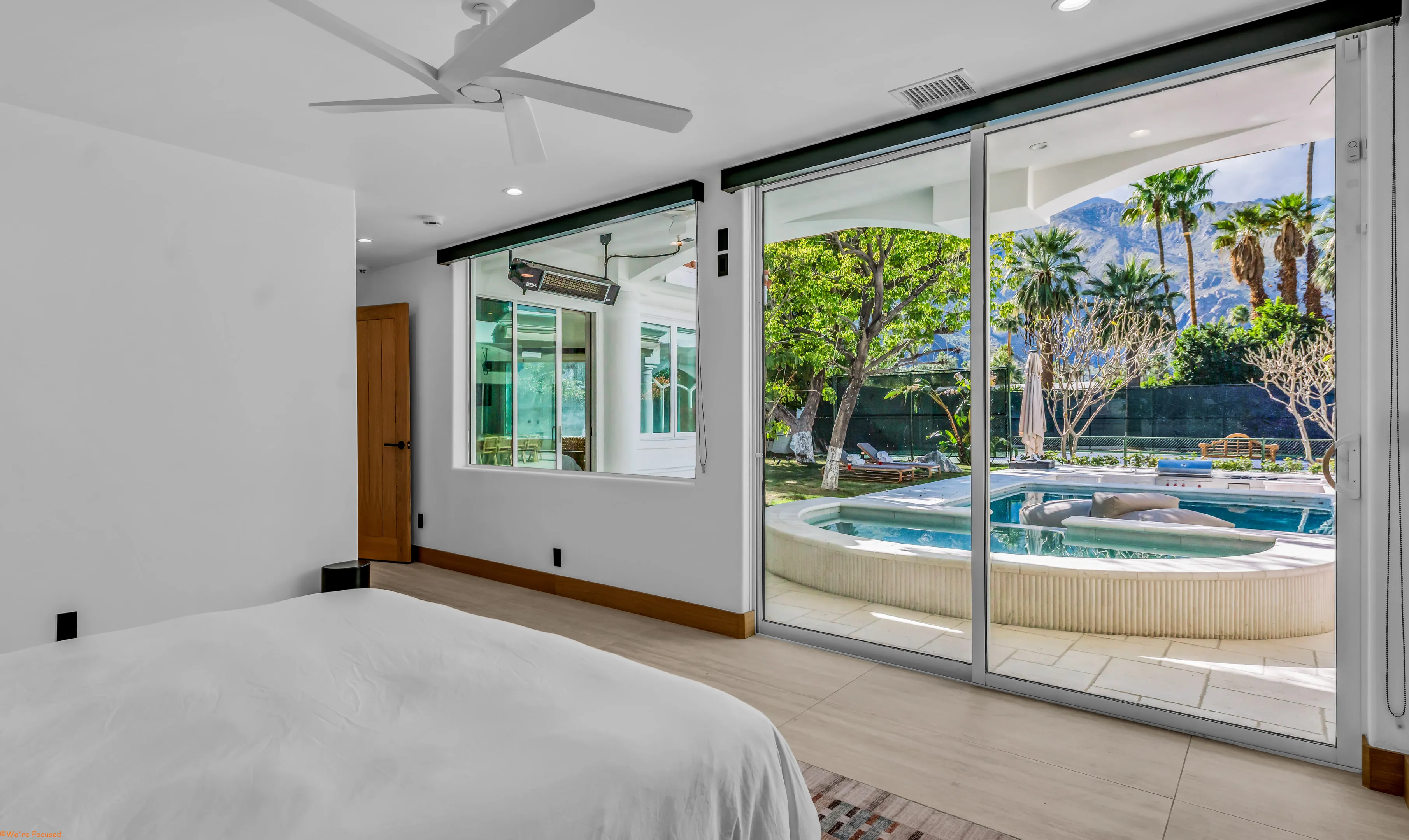 From the bed, sliding glass onto the pool terrace with palms and the mountains beyond.