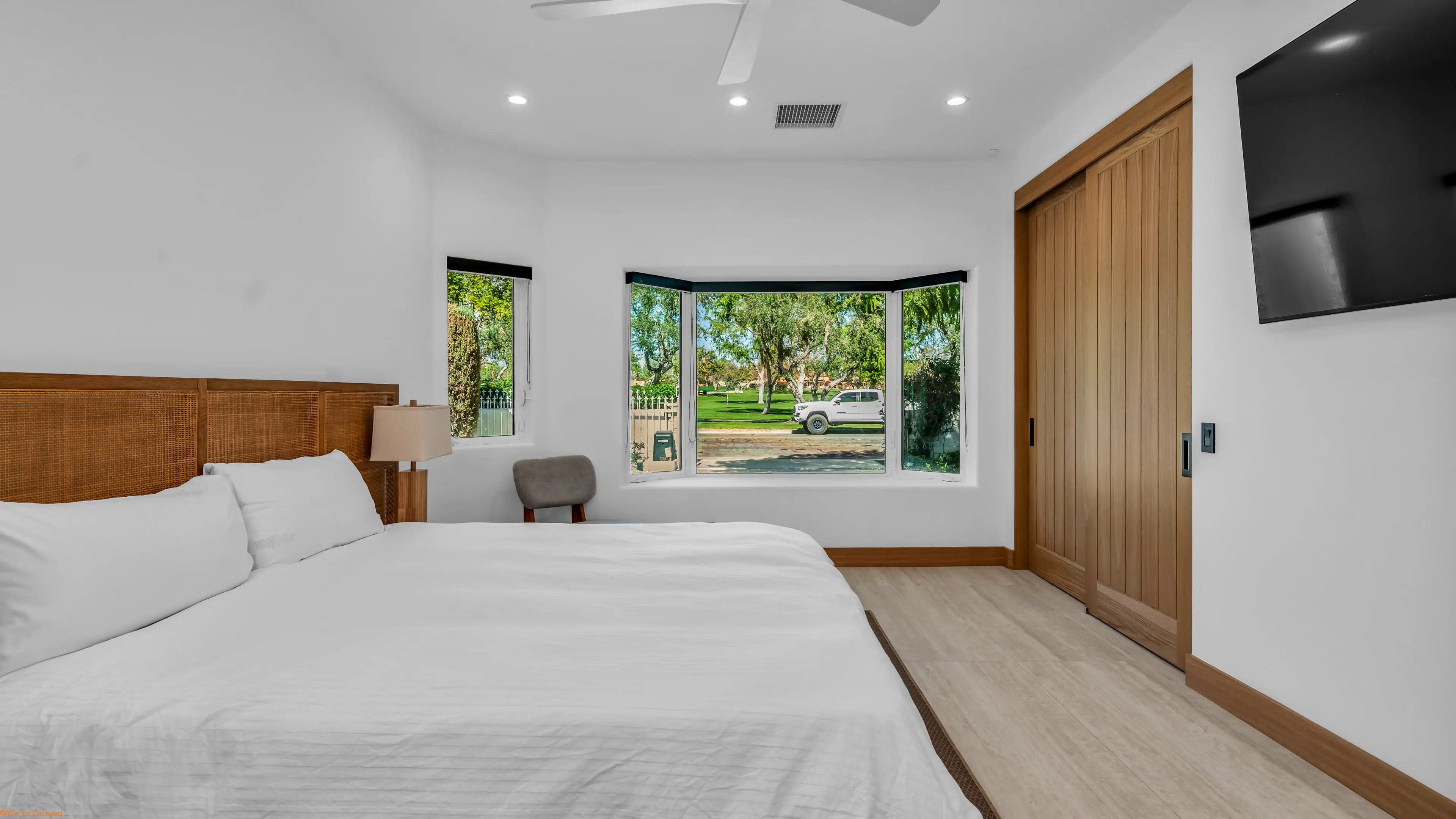 Bedroom with a cane headboard, a bedside lamp and a bay window onto the lawn and trees.