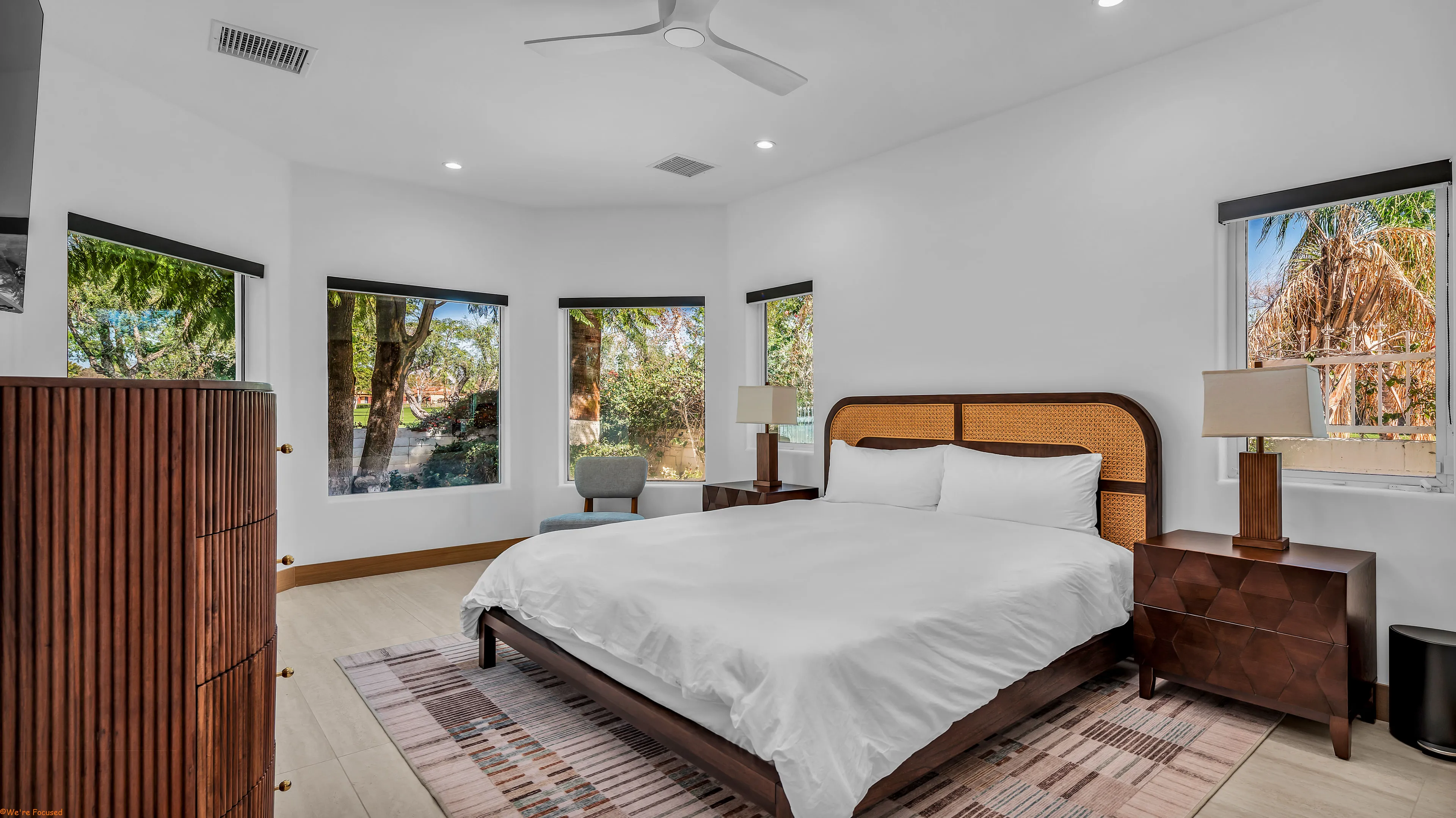 Bedroom with a cane headboard and bay windows on two sides looking into the trees.