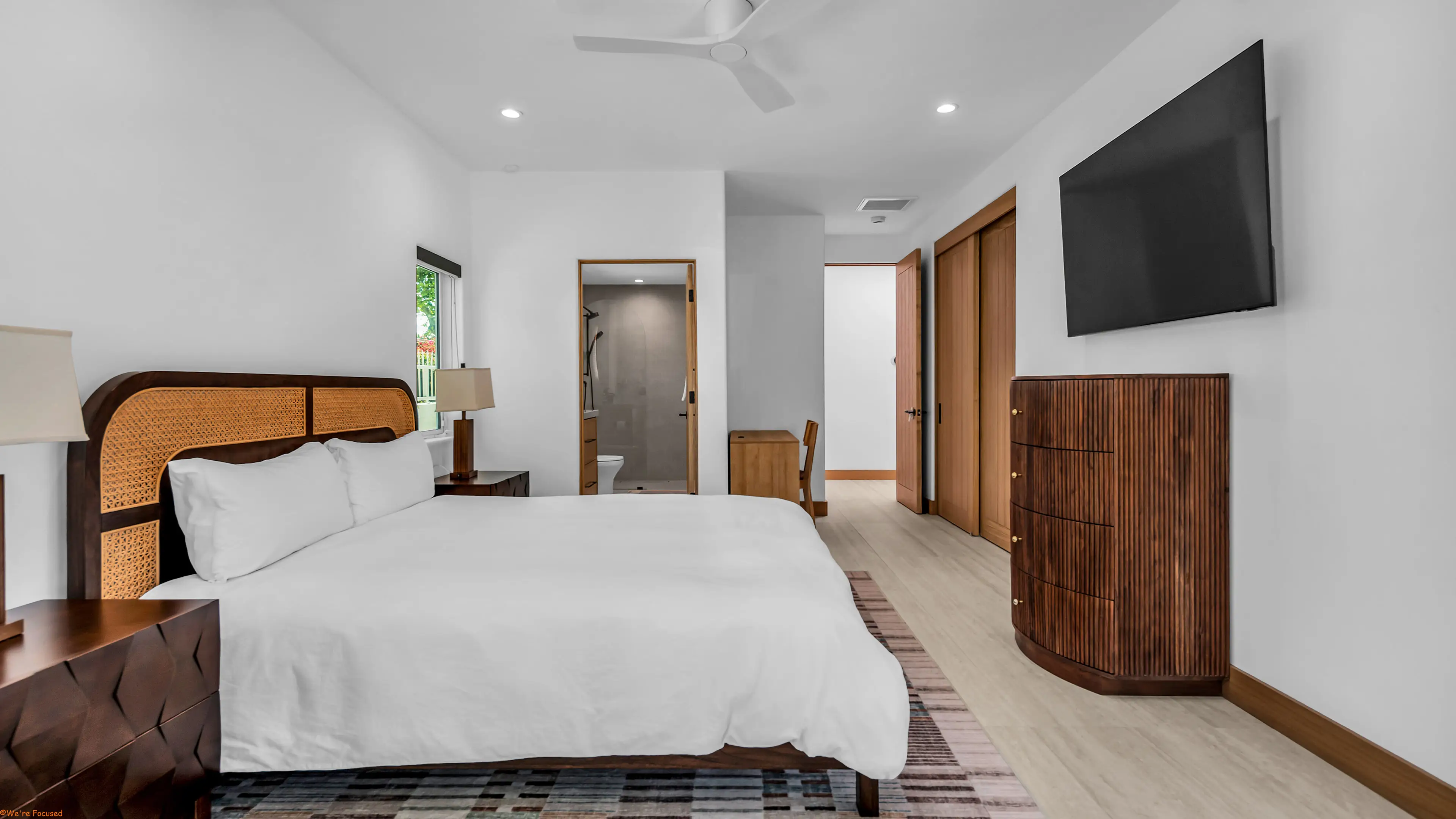 Bedroom with a cane headboard, a fluted wood dresser and a door to the bathroom.