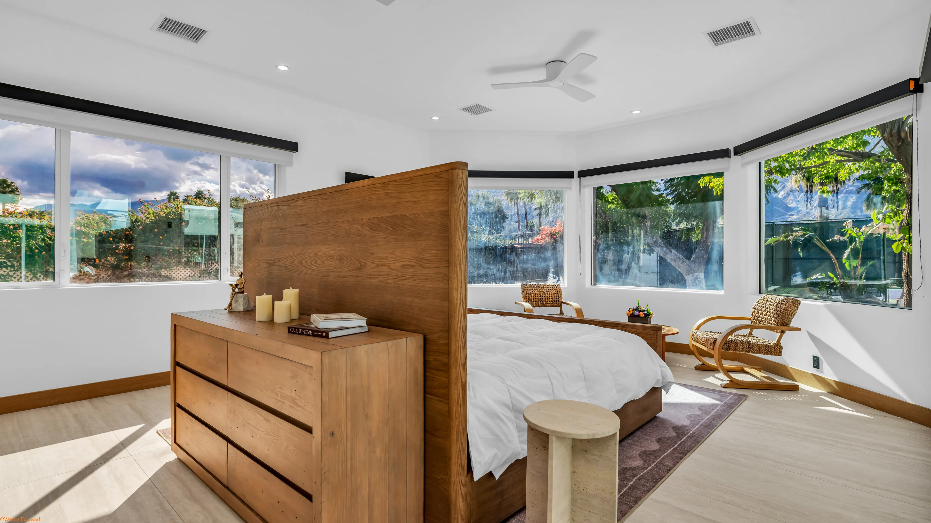 Bedroom with a tall wood headboard, an oak chest and bay windows on two sides.