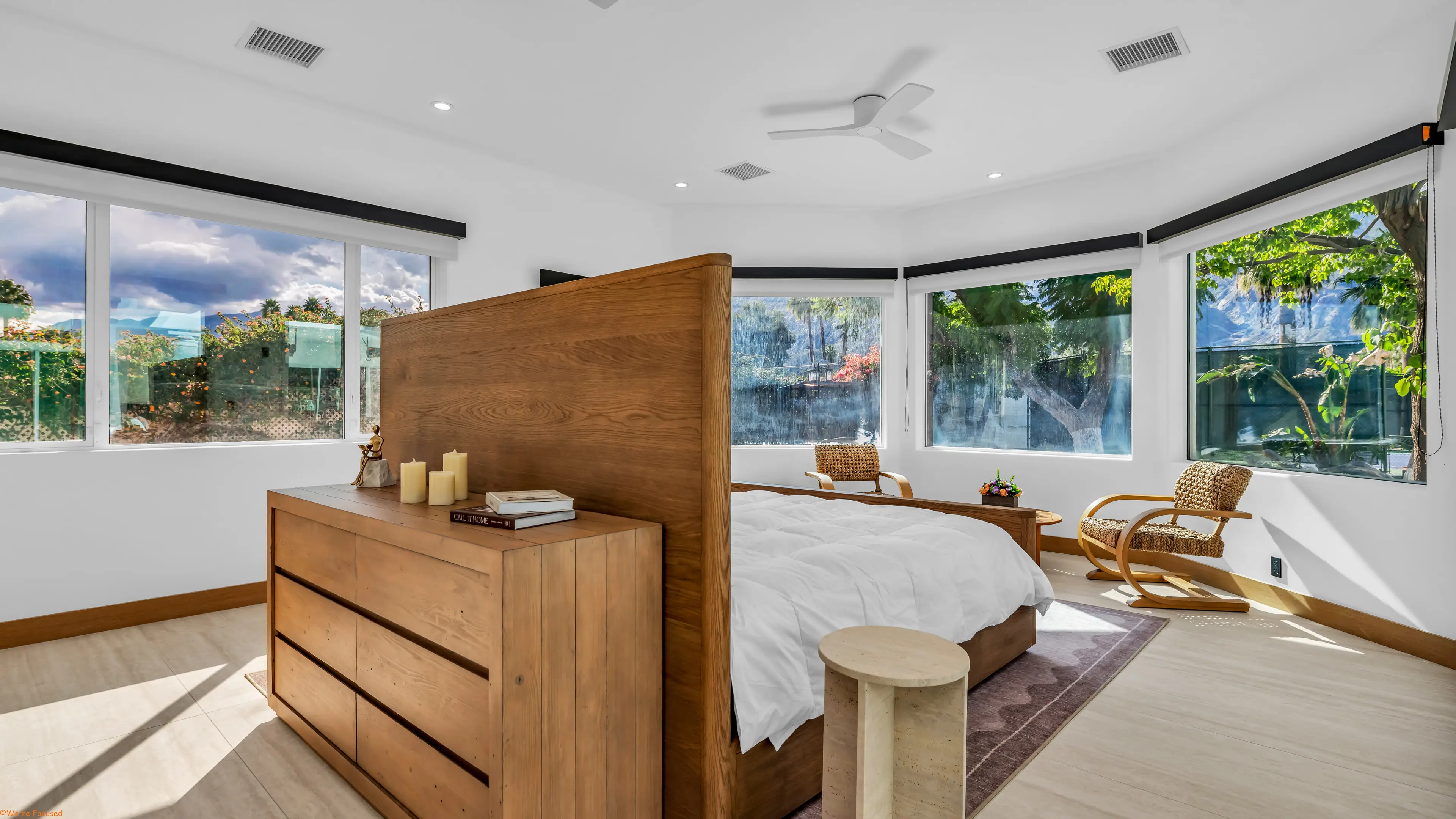 Bedroom with a tall wood headboard, an oak chest and bay windows on two sides.