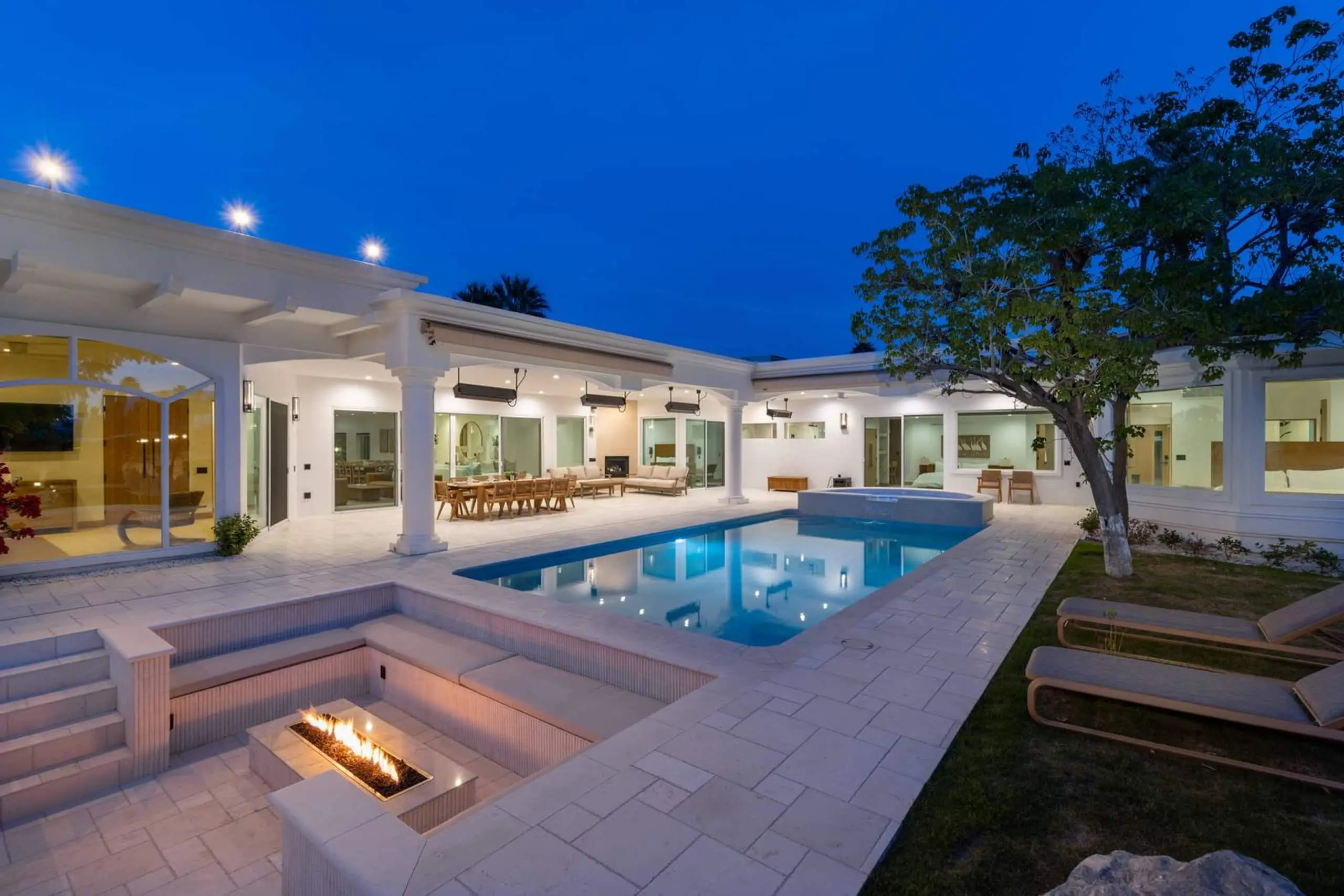 Blue hour. The pool lit from within, the sunken fire pit alight, and the house glowing along one side of the courtyard.