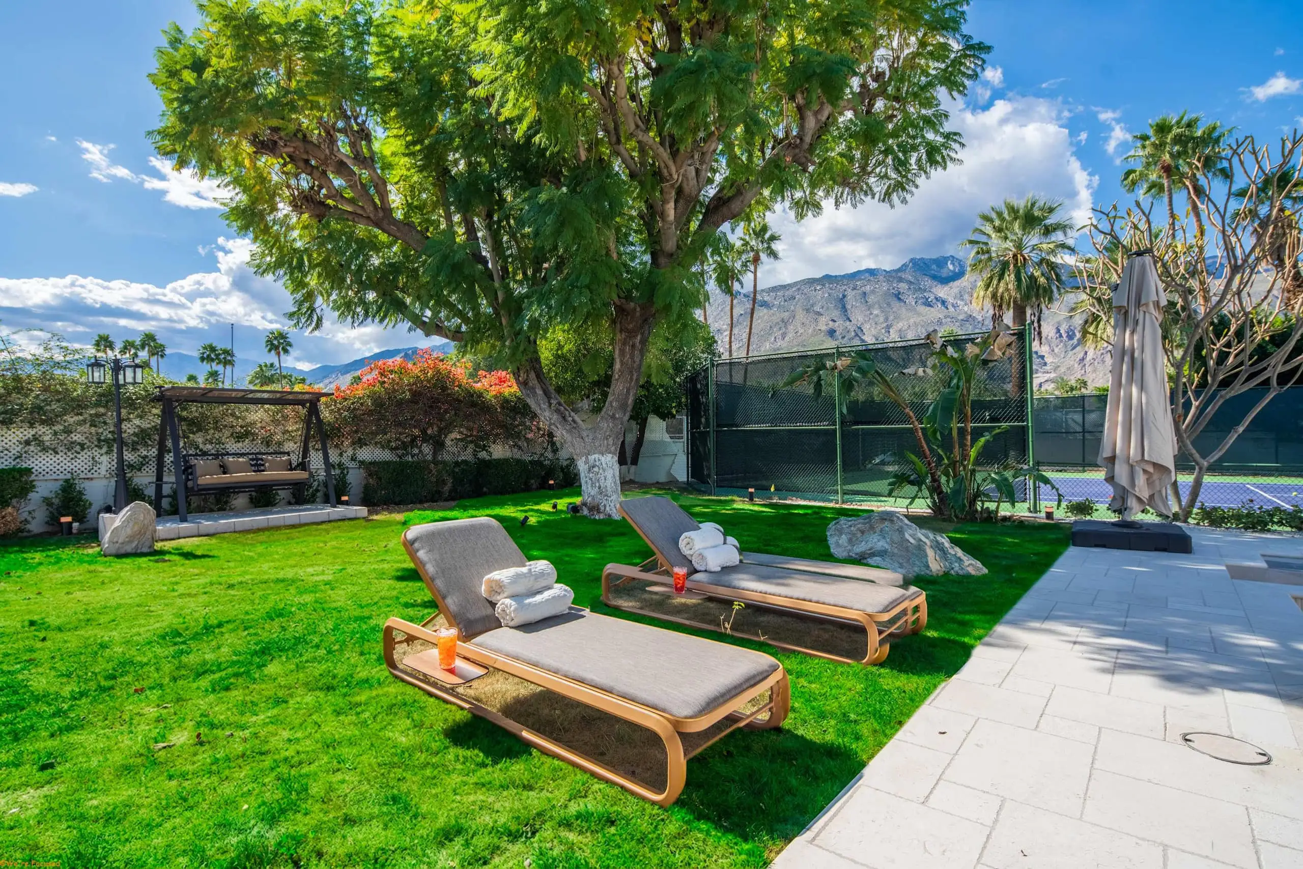 Loungers on the lawn with the tennis court fence and the mountains behind.