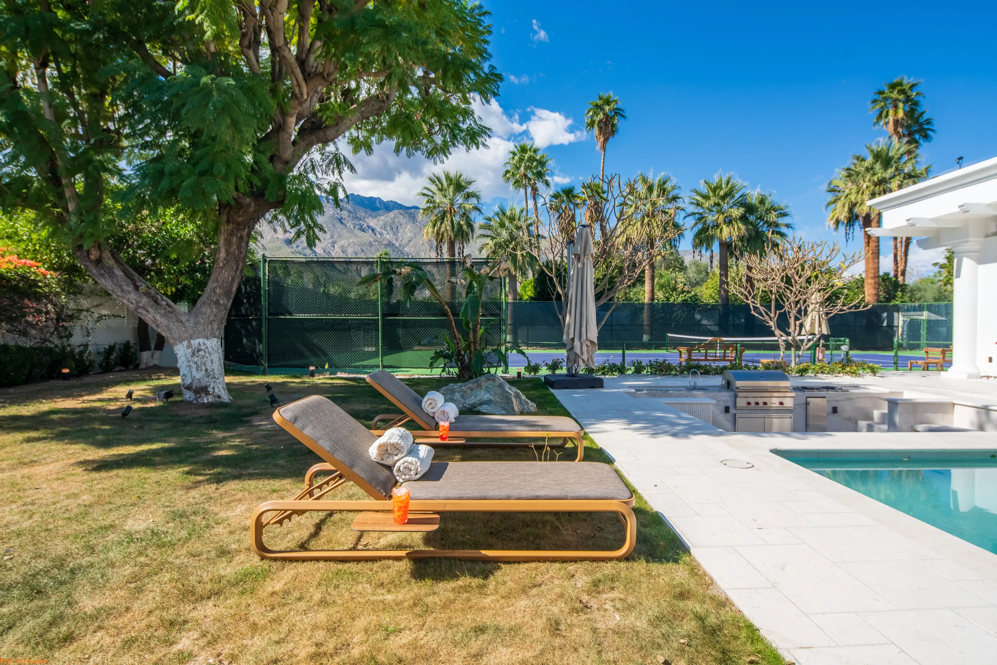 Loungers on the lawn beside the pool, with palms and the mountains behind.