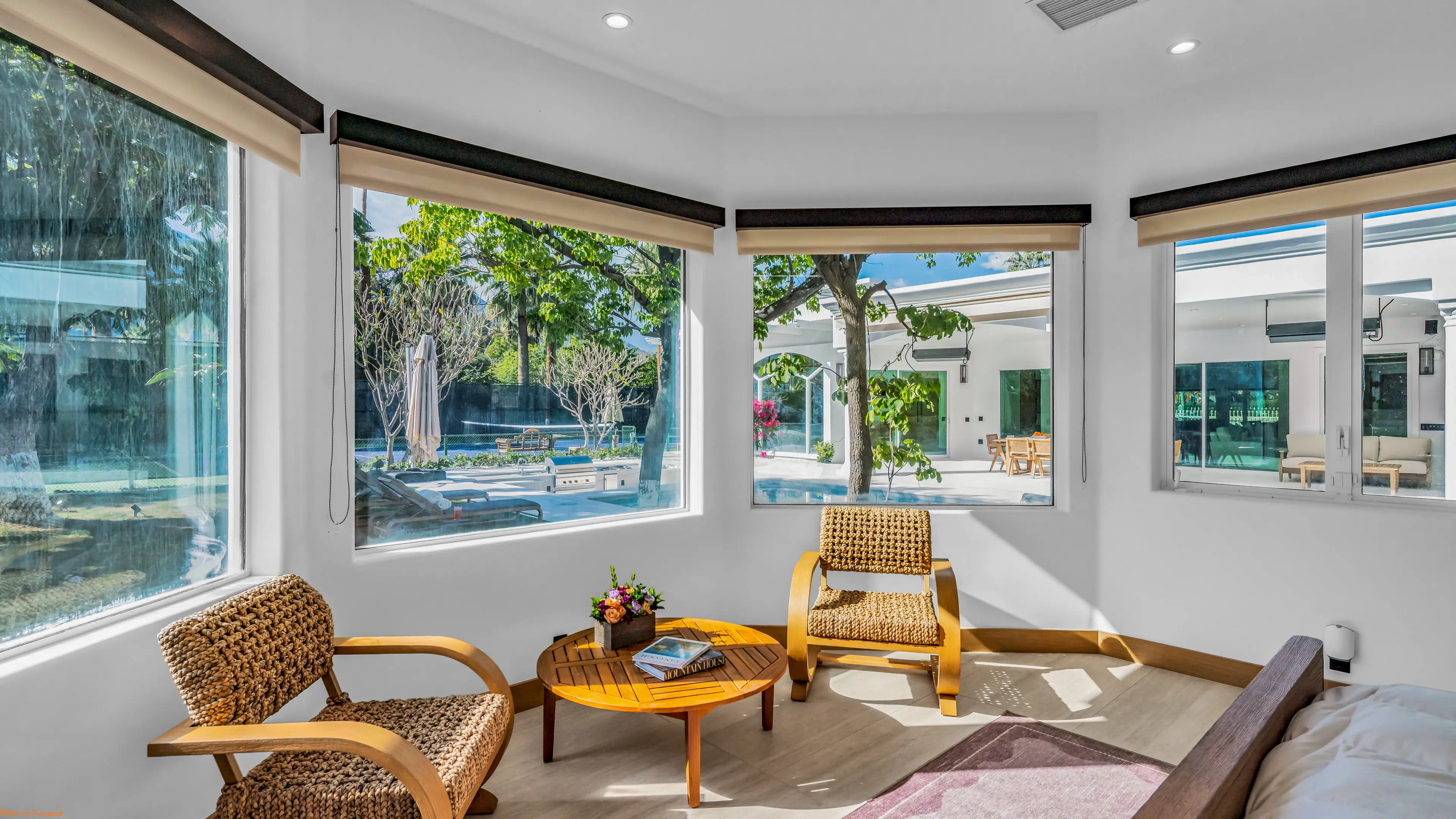 A sitting corner of woven chairs inside a bay window looking onto the pool.