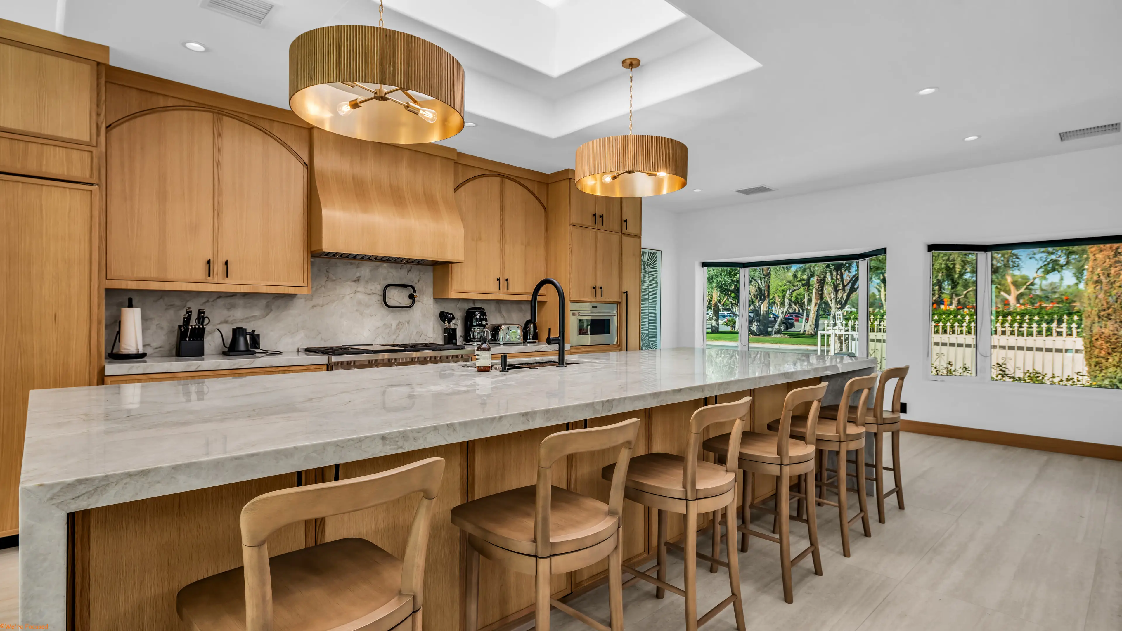 Kitchen with a marble island and seating for six, under drum pendants.