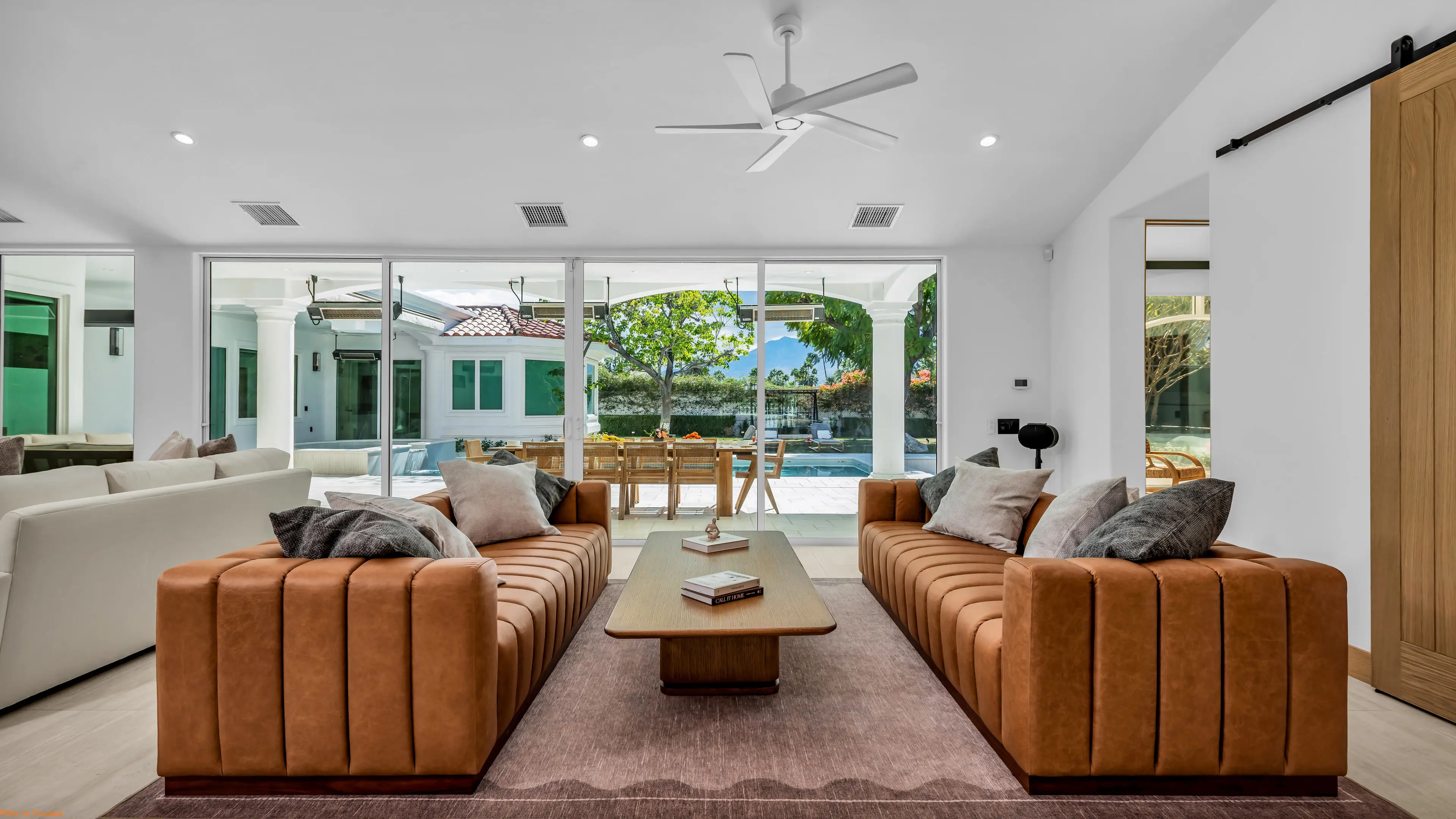 The great room with two facing leather sofas and the glass wall open to the pool terrace.