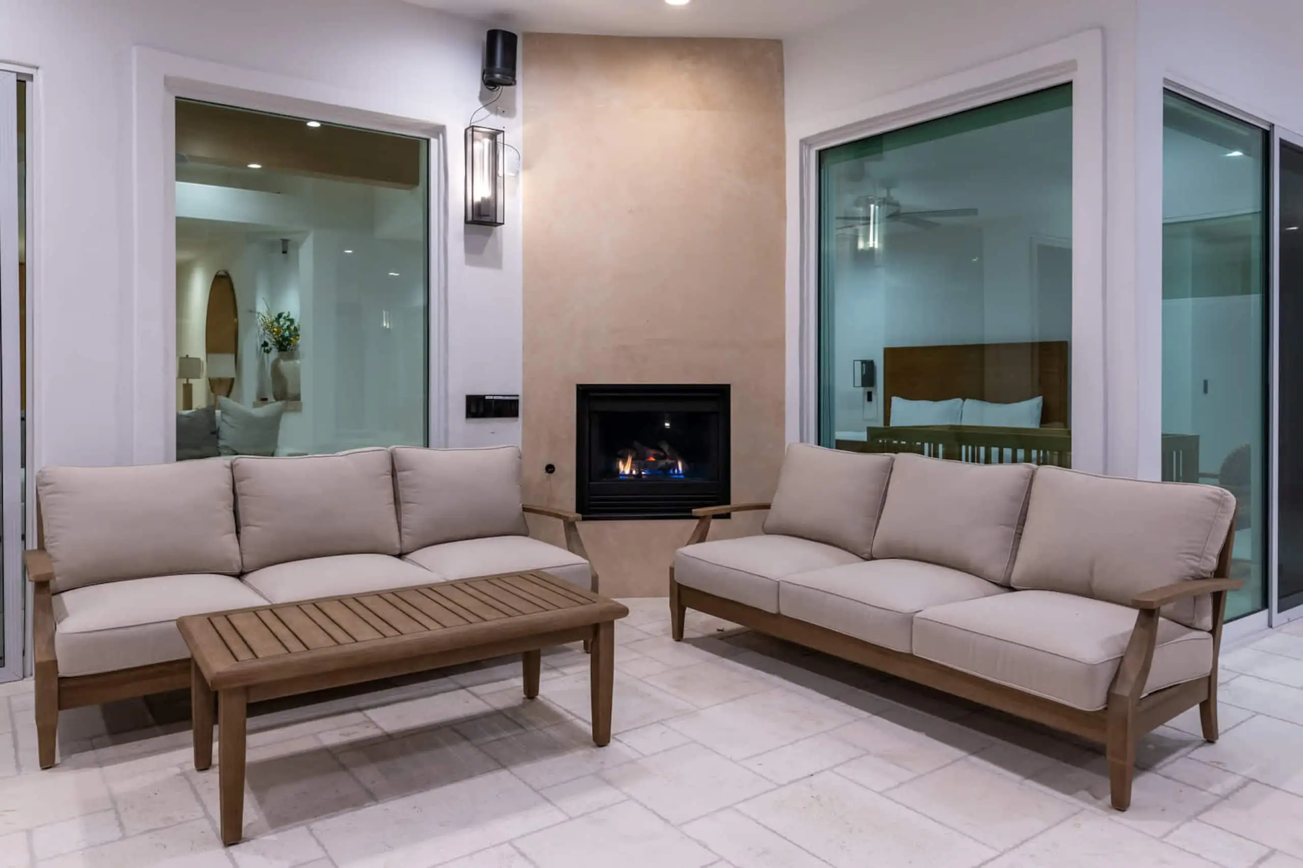 Teak sofas facing the outdoor fireplace under the colonnade, with the house through the glass behind.