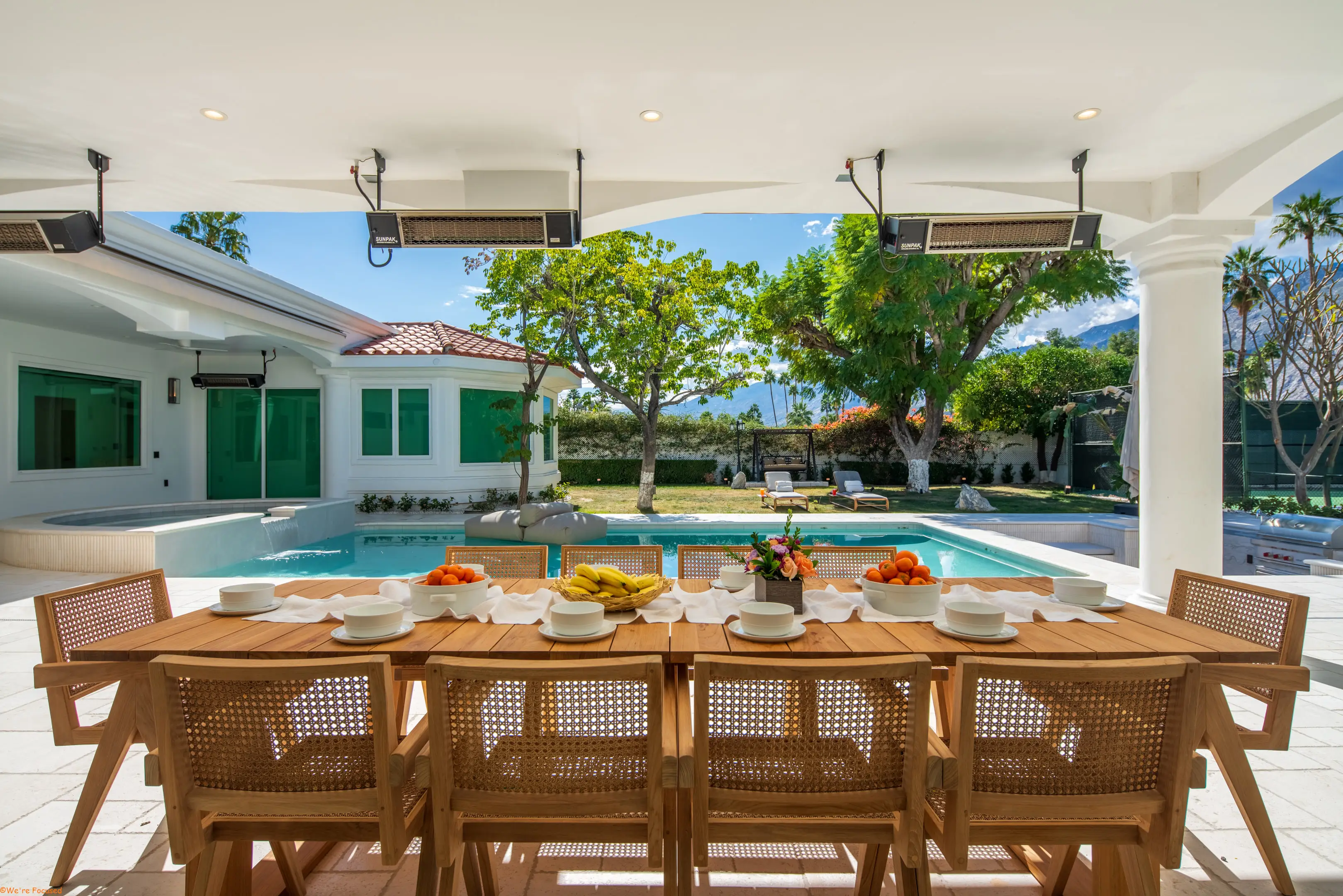 The outdoor table laid for a meal beside the pool, under the covered terrace.