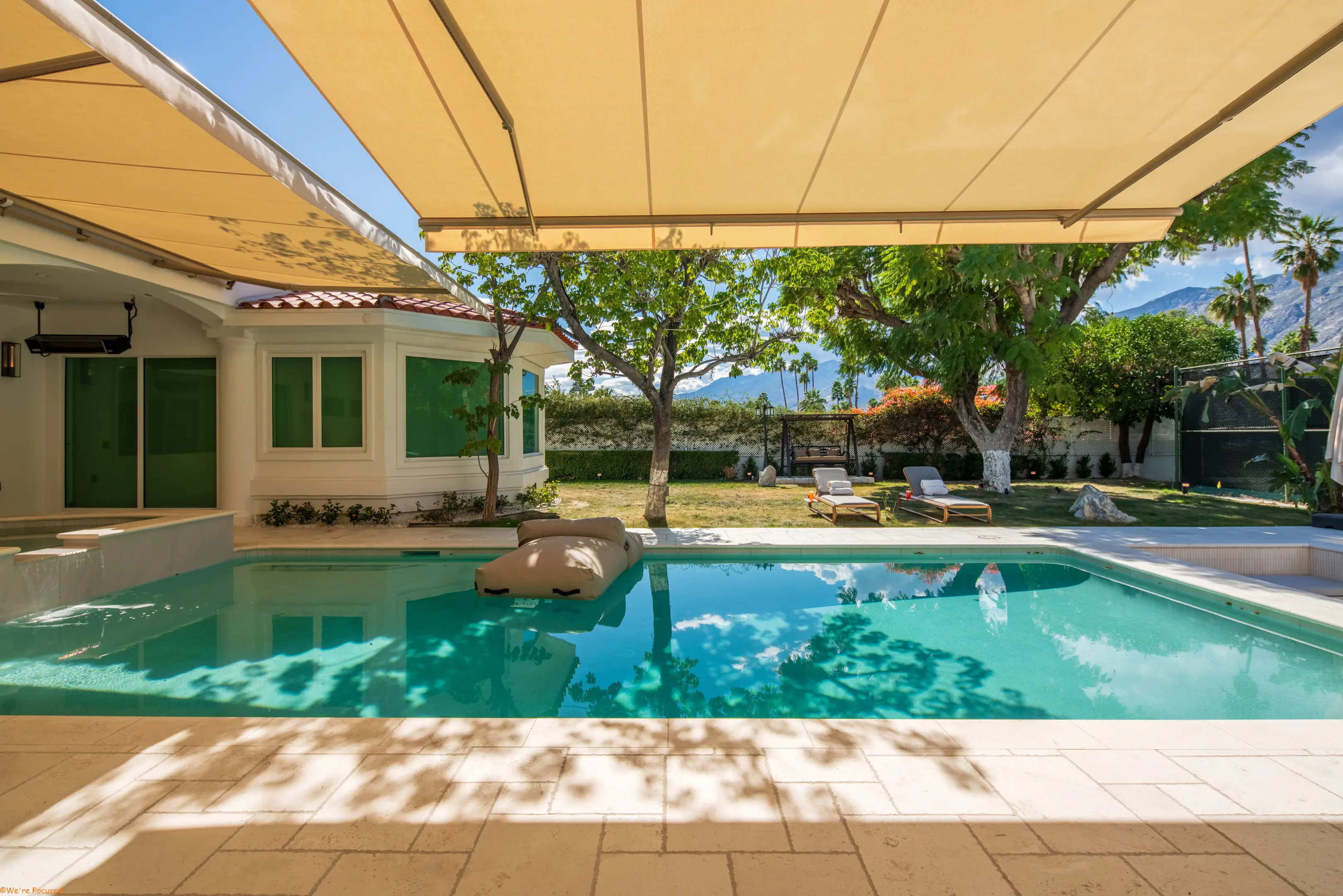 The pool seen from under the awning, its water turquoise against pale stone.