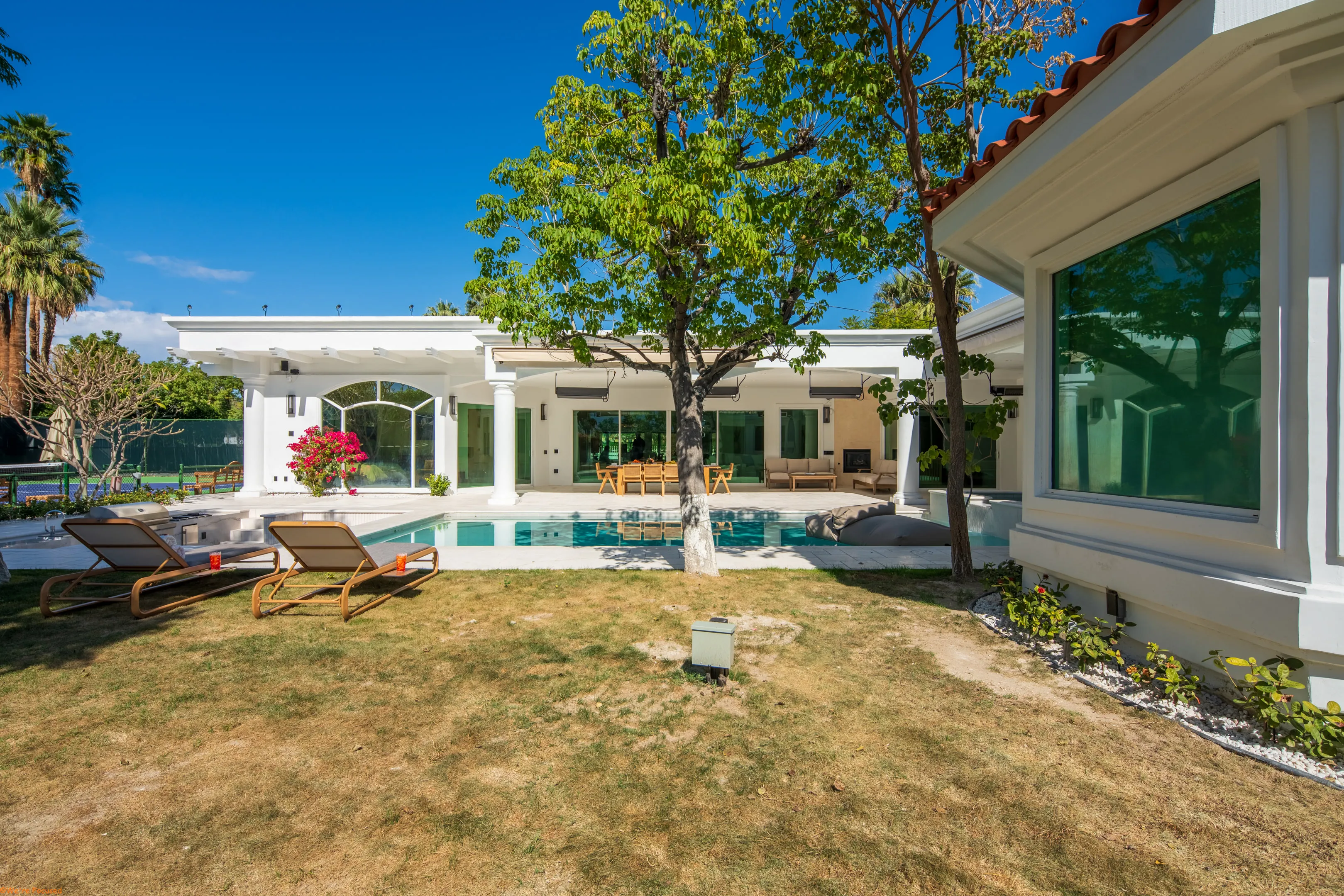 The house and pool seen across the lawn, framed by a mature tree.