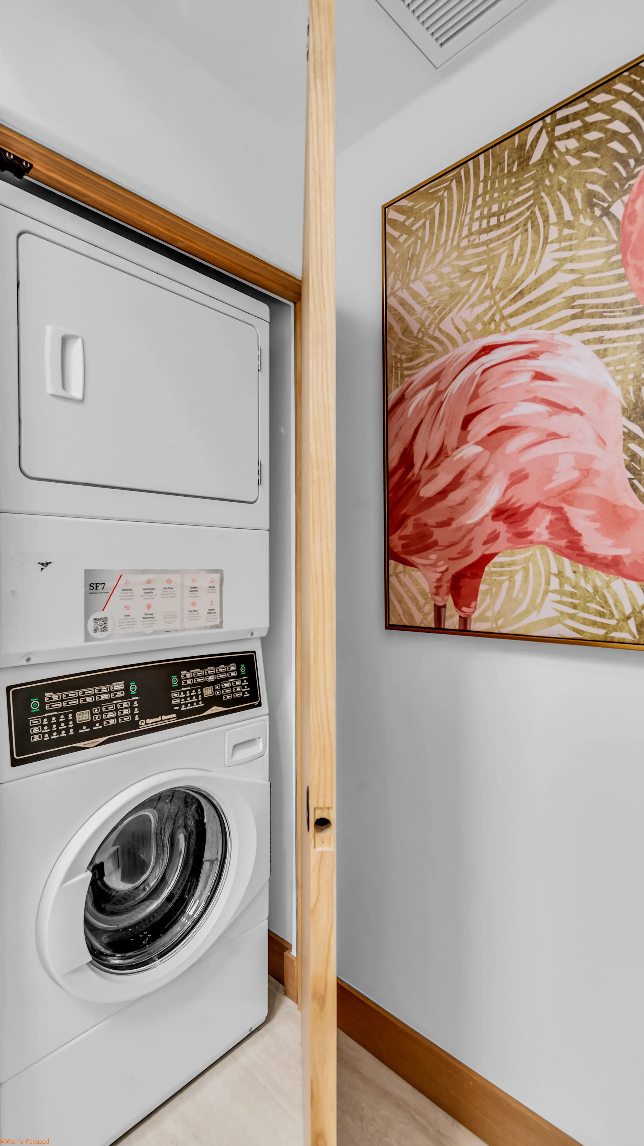 The laundry, with a stacked washer and dryer beside a painting.