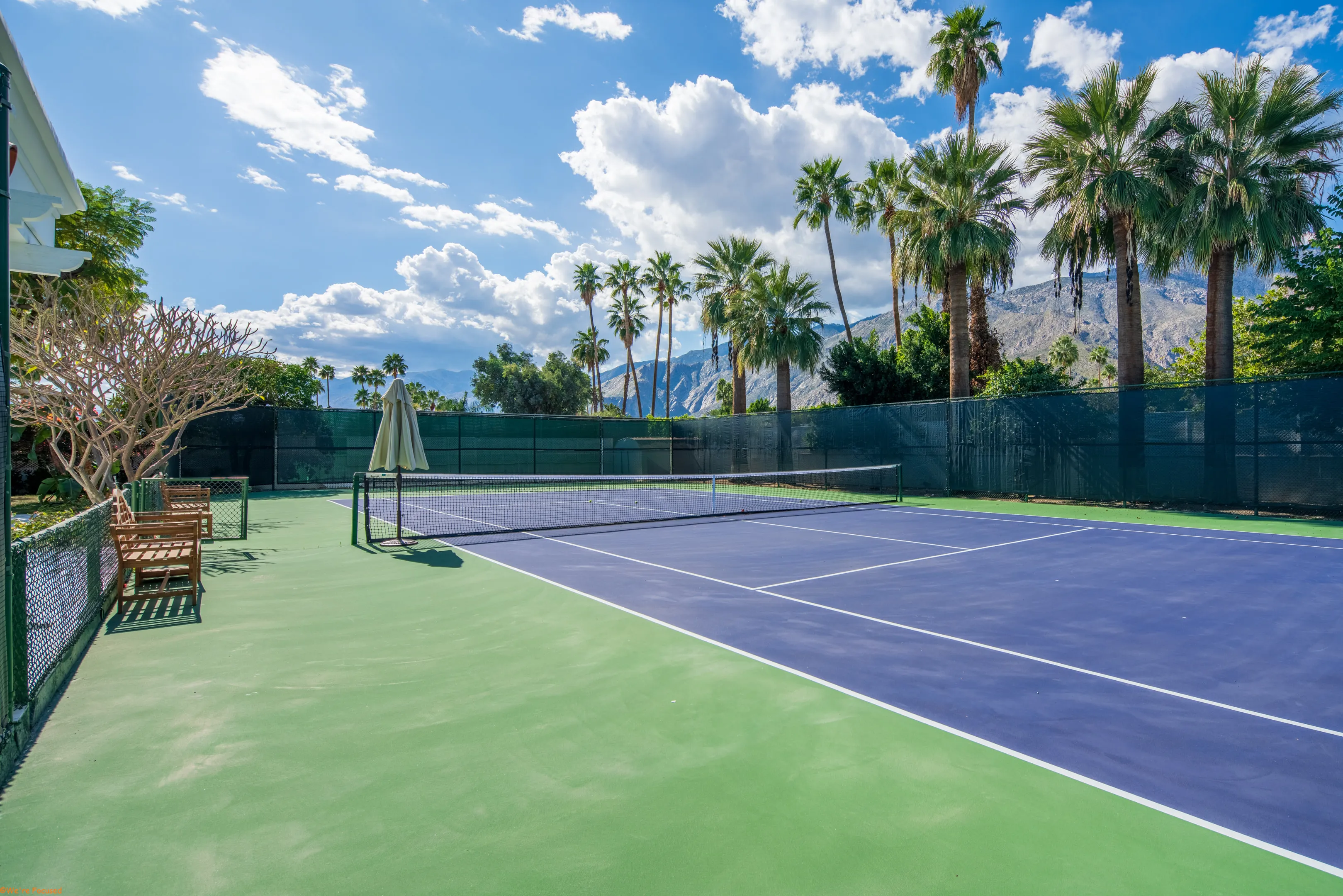 The tennis court from the baseline, the net and the far court clear under a wide sky.