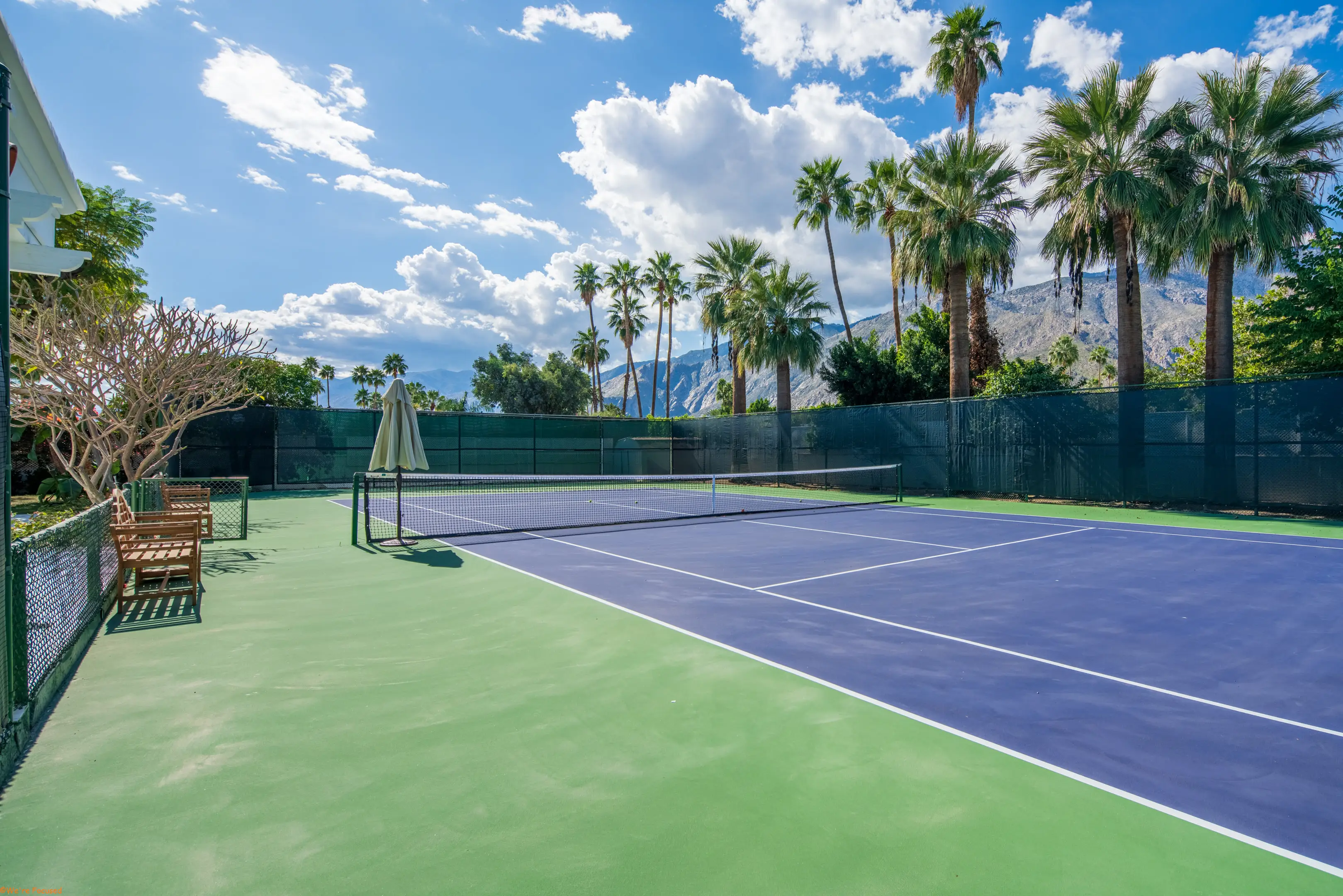The tennis court from the baseline, the net and the far court clear under a wide sky.