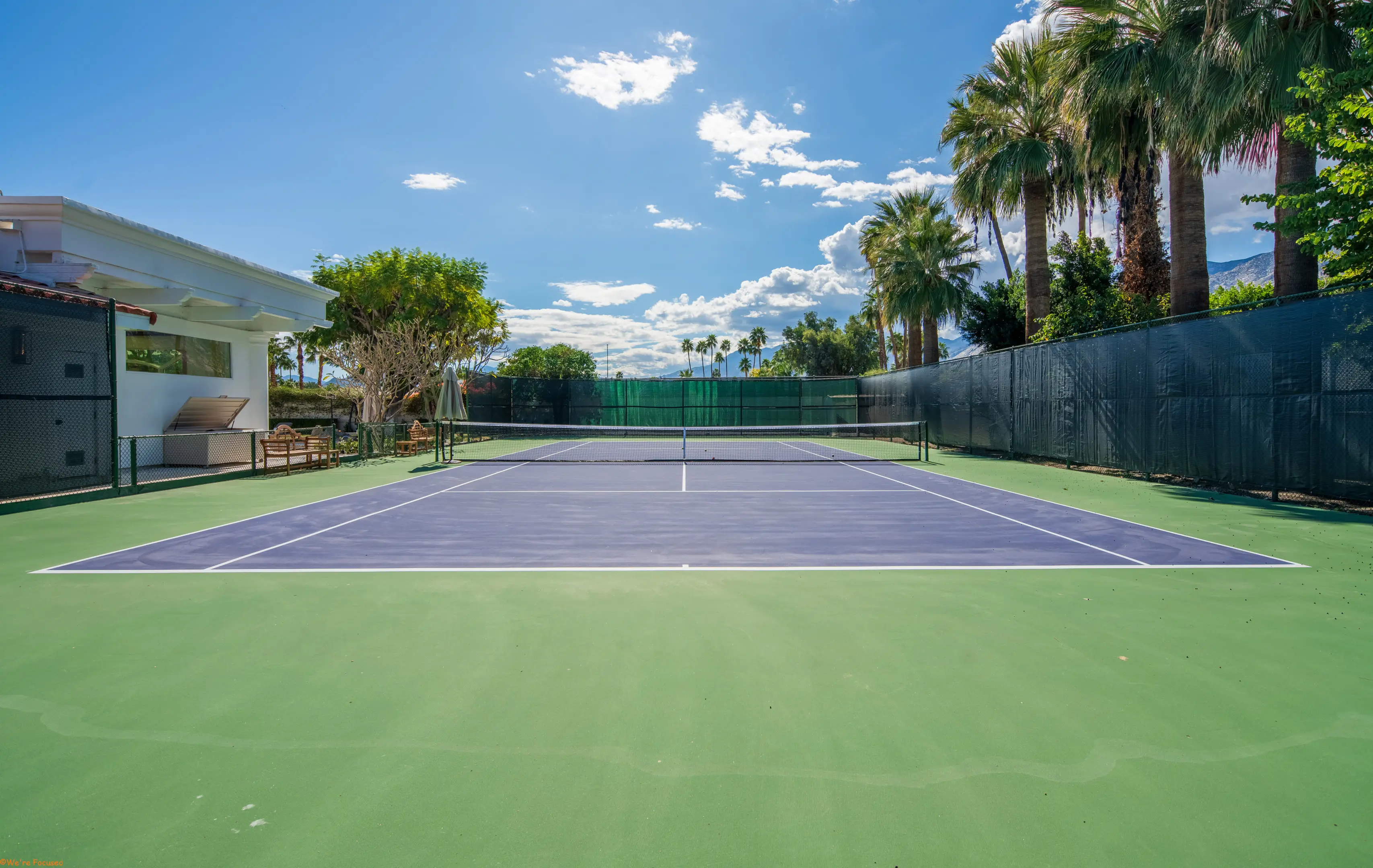 The full private tennis court, its blue surface and green surround set among palms below the mountains.